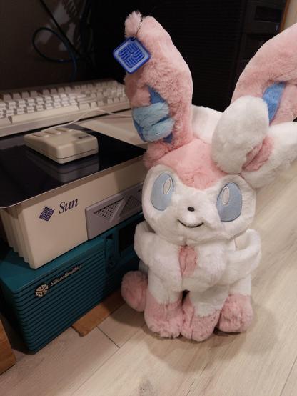 sylveon plush sitting next to a sun ultra enterprise 1 workstation, with a 3d printed sun logo keychain on its ear